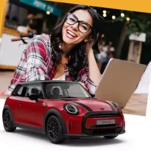 Man sieht eine junge Dame vor Ihrem Laptop. Darunter sieht man einen schicken Mini Cooper. Vielleicht hat die Damen das Auto als Abo gebucht und freut sich darüber.